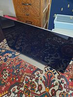 Front angled view of the Sony flat screen TV with base stand showing the screen and frame, placed on patterned carpet.