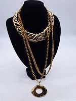 Front view of the three necklaces displayed on a black bust including chunky link, layered chain with pendant, and thick textured chain necklace