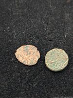 Top view of two ancient coins side by side on black fabric background, showing heavy wear and corrosion.