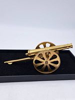 Side view of the brass model cannon showing the carriage, wheels and barrel