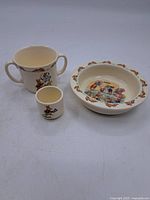 Three Bunnykins ceramic items: handled cup, egg cup, shallow bowl with bunny illustrations.