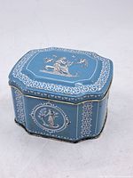 Closed view of the blue vintage English tin box showing decorative classical figures and white border patterns on the exterior.