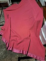 Full view of the red wool blanket with visible satin trim along one edge, laid out over a dark surface.