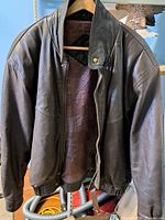 Front view of the vintage brown leather men's jacket hanging on a hanger, showing zip closure and snap button collar.