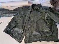 Full view of the vintage men's leather jacket laid flat, showing body, sleeves, and front flap pockets with snap buttons and elastic waistband and cuffs.