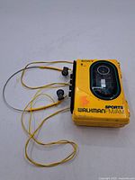 Yellow Sony Walkman Sports FM/AM cassette player with attached headphones laid flat showing cassette window and cables.