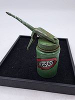 Front view of the vintage Wesco greaser/oiler showing the Wesco label on green metal body with visible rust and wear.