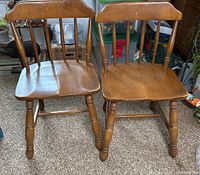 Pair of wooden chairs with straight backs, spindle supports, and turned legs showing scratches on the seating surfaces.