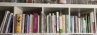 Books on a white shelf including various cookbooks arranged upright showing their spines with a variety of titles surrounding cooking and diets.