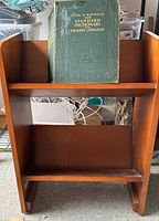 Wooden dictionary stand holding the large dictionary on top shelf with lower shelf empty, cables stored on lower shelf.