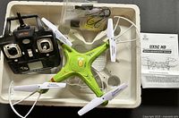 Complete drone set including green drone, black remote, manual, and charging cable in foam tray