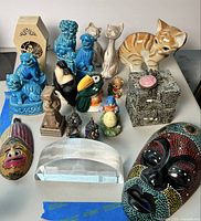 Overview of all figurines, paperweight, decorative box, and mini masks arranged on table with clear background.