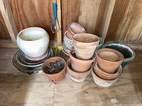 Clay and ceramic pots stacked and arranged inside wooden shed, includes white glazed, terracotta and beige pottery with some dirt inside