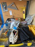 Overview photo of assorted hardware, hand tools, canvas pouches, plastic organizers, caulking gun, and mesh roll on a pegboard background.