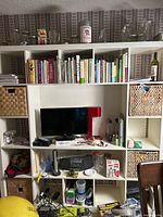 Front view of the white IKEA Billy bookcase filled with books, baskets, a small TV, and various other household items.