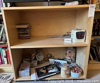 Front view of the open-faced light wood TV stand/bookcase showing two compartments with various personal items on shelves.
