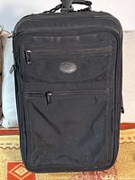 Front view of black Kirkland roller bag showing two zippered compartments and a central oval Kirkland logo patch.