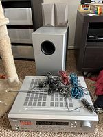 Full view of Onkyo AV receiver with SKW-8230 powered subwoofer behind and two bookshelf speakers on top. Multiple cables and antenna wire are on the receiver showing included accessories.