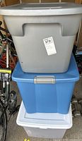 Stacked view of three large plastic storage bins in gray, blue, and translucent white.