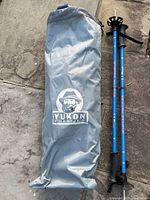 Grey Yukon Charlie branded carrying bag and blue Yukon Charlie walking poles on stone background.