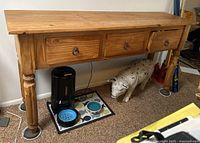 Full view of wooden side table with three drawers, showing the entire piece including the legs and top surface. Visible damage on left leg and edges.