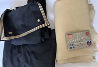 Photo showing the navy uniform sailor jumper folded, the wool blanket rolled, and the insignia booklet on top of the blanket.