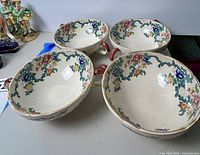 Four vintage Royal Cauldon two-handled soup bowls with a floral design arranged on a table.