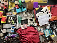 Assorted household and office items including fabric yard flags, aprons, shoelaces, fasteners, bookends, calculator, stapler, and more.