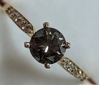 Top-down close-up of round natural diamond center stone showing facets and pavé-set side diamonds