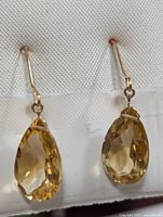 Front close-up view of both 14KT gold and citrine drop earrings placed on a white fabric background.