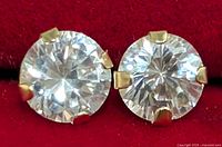 Close-up photo showing round faceted cubic zirconia stones set in 14KT gold prongs against a red background.