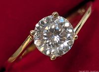 Close-up image of the ring showcasing the round moissanite stone set in 10KT yellow gold with four prongs.