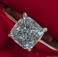 Close-up top-down view of cushion cut lab-grown diamond set in four-prong 10k white gold ring on red fabric