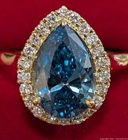 Front view of pear-shaped blue centre diamond with surrounding halo on red background