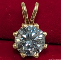 Front view of gold pendant on red fabric background showing diamond and bail