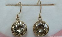 Front view of both earrings hanging from display rod, showing round faceted moissanite stones in bezel settings