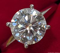 Front close-up of round brilliant moissanite in four-prong setting on a polished white-gold band