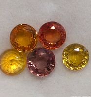 Five round cut sapphires in various fancy colors shown together on a white background.