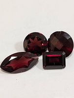 Four garnet gemstones with different cuts including marquise, round brilliant, round, and rectangular emerald cut displayed on white background.
