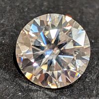 Close-up photo of round cut moissanite gemstone displaying its facets and brilliance on a black background.