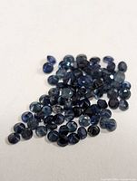 Cluster of loose round-cut blue sapphire gemstones showing various dark blue shades and faceted surfaces.