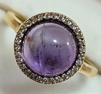 Close-up of the amethyst cabochon ring with halo of clear stones, showing the purple stone and silver band
