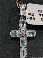 Front view of silver pendant with five oval blue topaz stones arranged in a cross shape with tag showing weight and gem type.