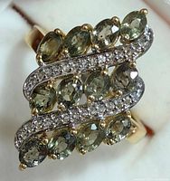 Close-up image of the ring showing oval green sapphires and white topaz stones in a wavy design on silver band with gold accents.