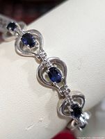 Close-up of sterling silver bracelet links showing oval-cut deep blue iolite gemstones set in heart-shaped silver frames with silver bead detailing.