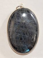 Front view of oval labradorite pendant with visible blue iridescence and natural veining, set in plain silver bezel.