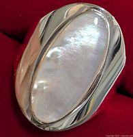 Close-up front view of silver ring with polished elongated oval mother of pearl inlay on red velvet background.