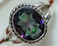 Close-up view of silver ring featuring oval-shaped Mystic Topaz stone with visible faceted cut and multi-color reflections. Rope bezel detailing visible.