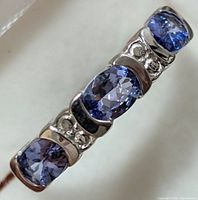 Close-up front view of silver ring with three cushion-cut tanzanite stones and small clear accent stones between each gemstone.