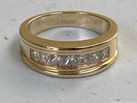 Front view of ring on flat surface showing gold band and channel set princess cut diamonds.